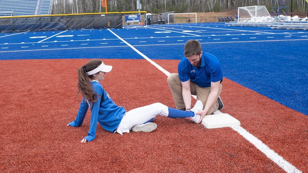 A student checks the ankle of a U N E softball player