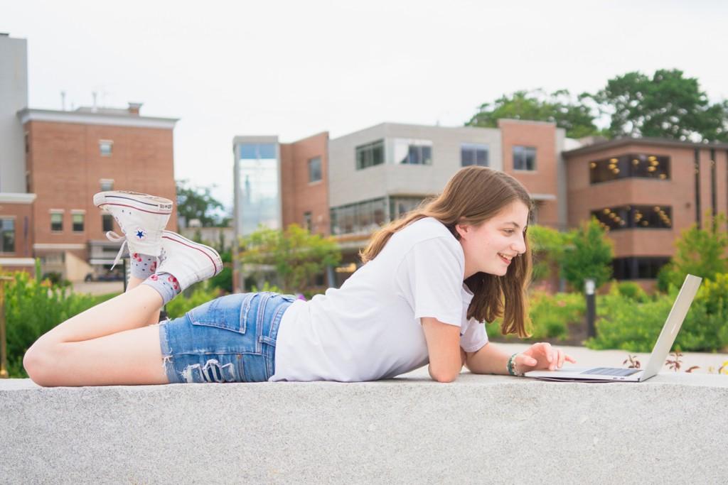 A student using their laptop while laying outside