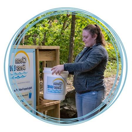 A student brings a filled Clean Seas U N E bucket to the drop-off location on the Biddeford Campus