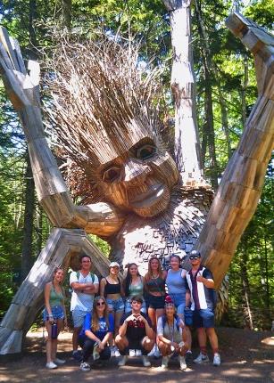 A group of U N E students stand in front of a giant troll installation at the Maine Botanical Gardens