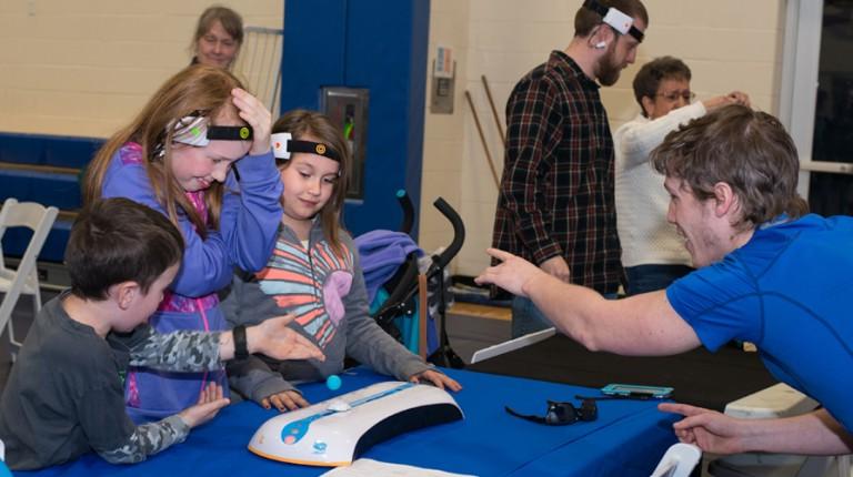 A student explains technology to three children at a U N E Brain Fair