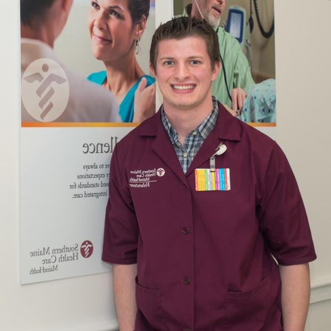 A U N E student wearing a colorful badge stands in front of a Southern Maine 健康 Care poster